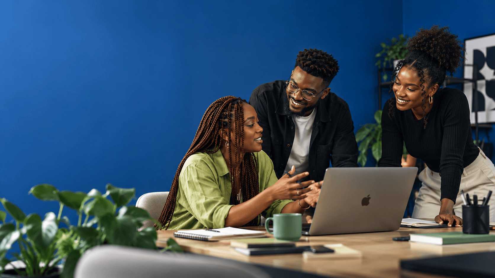 Three teammates sharing ideas around a laptop in a blue studio.